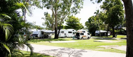 Un camping con vehículos recreativos y remolques estacionados en zonas verdes, rodeado de árboles.