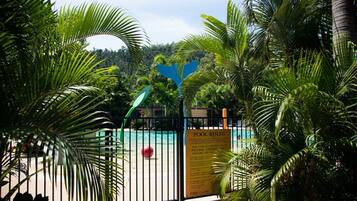 A pool area with a sign indicating pool rules, surrounded by lush greenery and a fence.