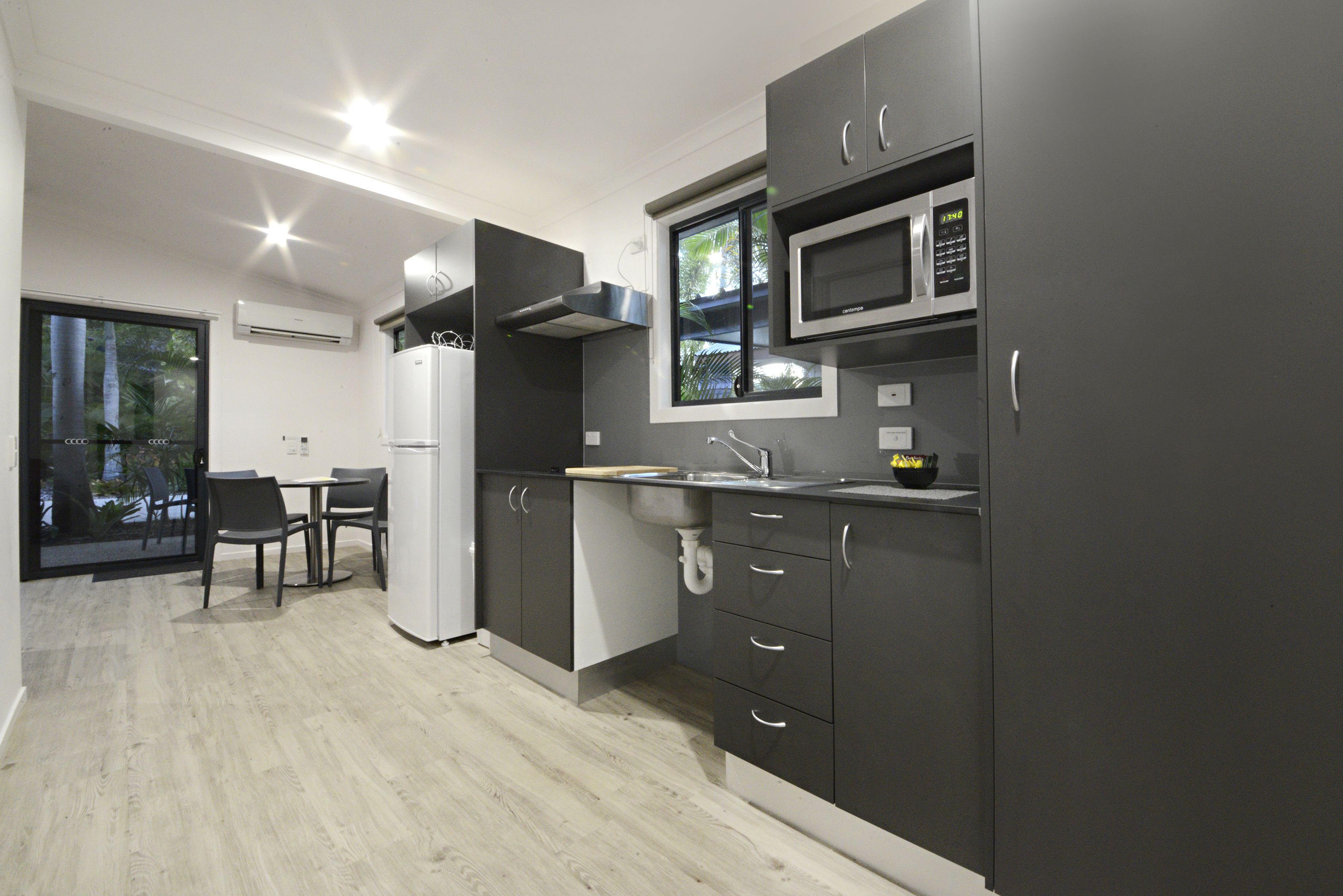 A modern kitchen with grey cabinets, a microwave, and a sink. There is a dining area with a table and chairs.