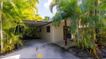 A house with a covered porch, surrounded by lush tropical vegetation.