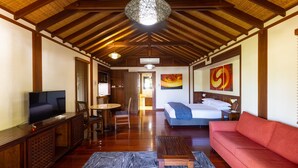Een ruime kamer met houten plafond, een televisie, een bank, een bed en kunstwerken aan de muren.