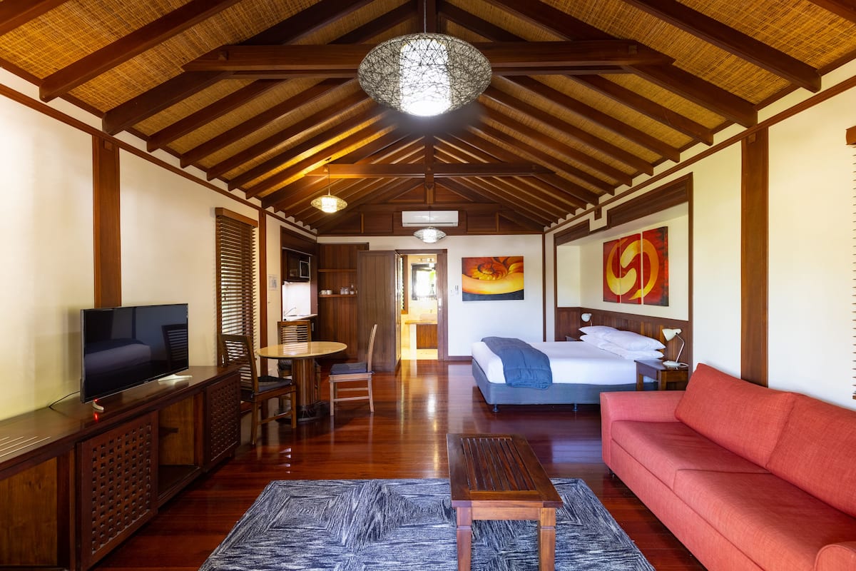 Quarto espaçoso com teto de madeira, televisão, sofá, cama e obras de arte nas paredes.