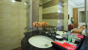 Une salle de bain avec un lavabo noir, une douche et un miroir. Un vase rempli de fleurs est posé sur le comptoir du lavabo.