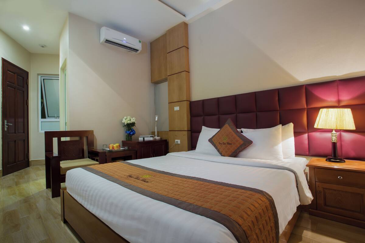 Ein Hotelzimmer mit einem großen Bett, einem Nachttisch mit Lampe, einem Holzschrank und einer Klimaanlage.