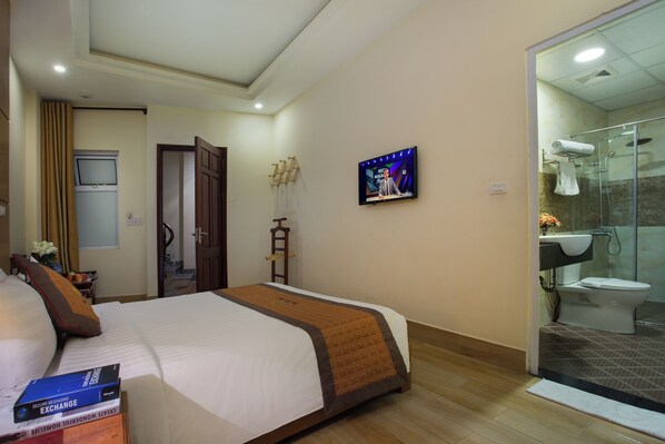 A hotel room with a bed, a television, a shower, and a small table with a vase of flowers.
