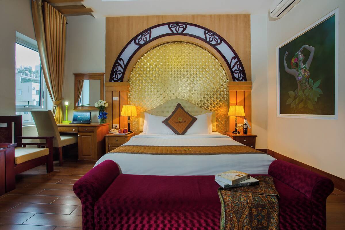 Ein Hotelzimmer mit einem großen Bett, einem Schreibtisch, einem Sessel und einem Fernseher.
