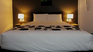 A hotel room with a bed, two bedside lamps, a wall-mounted artwork, and a door. - Parnell Pines (Auckland)