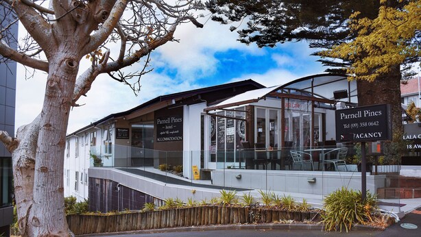 A modern hotel with a glass facade, outdoor seating, and a sign indicating availability. - Parnell Pines (Auckland)