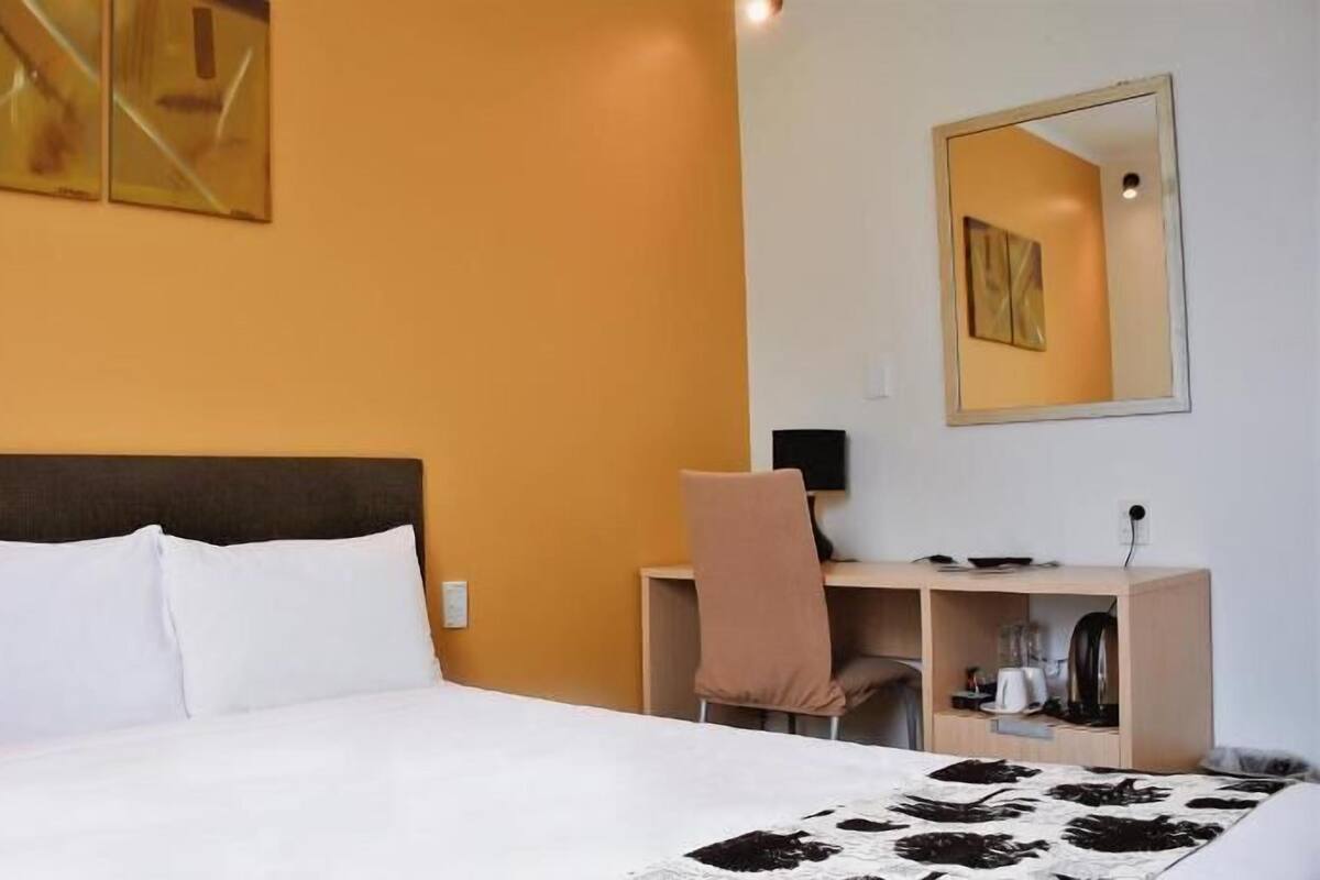 A hotel room with a bed, a desk, a chair, a mirror, and a coffee machine.