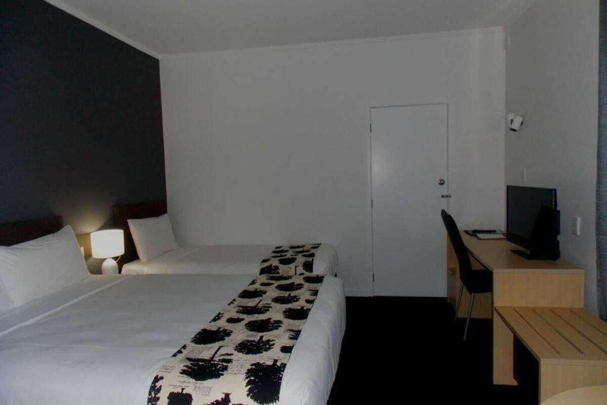 A hotel room with a bed, a desk, a chair, a television, and a door.
