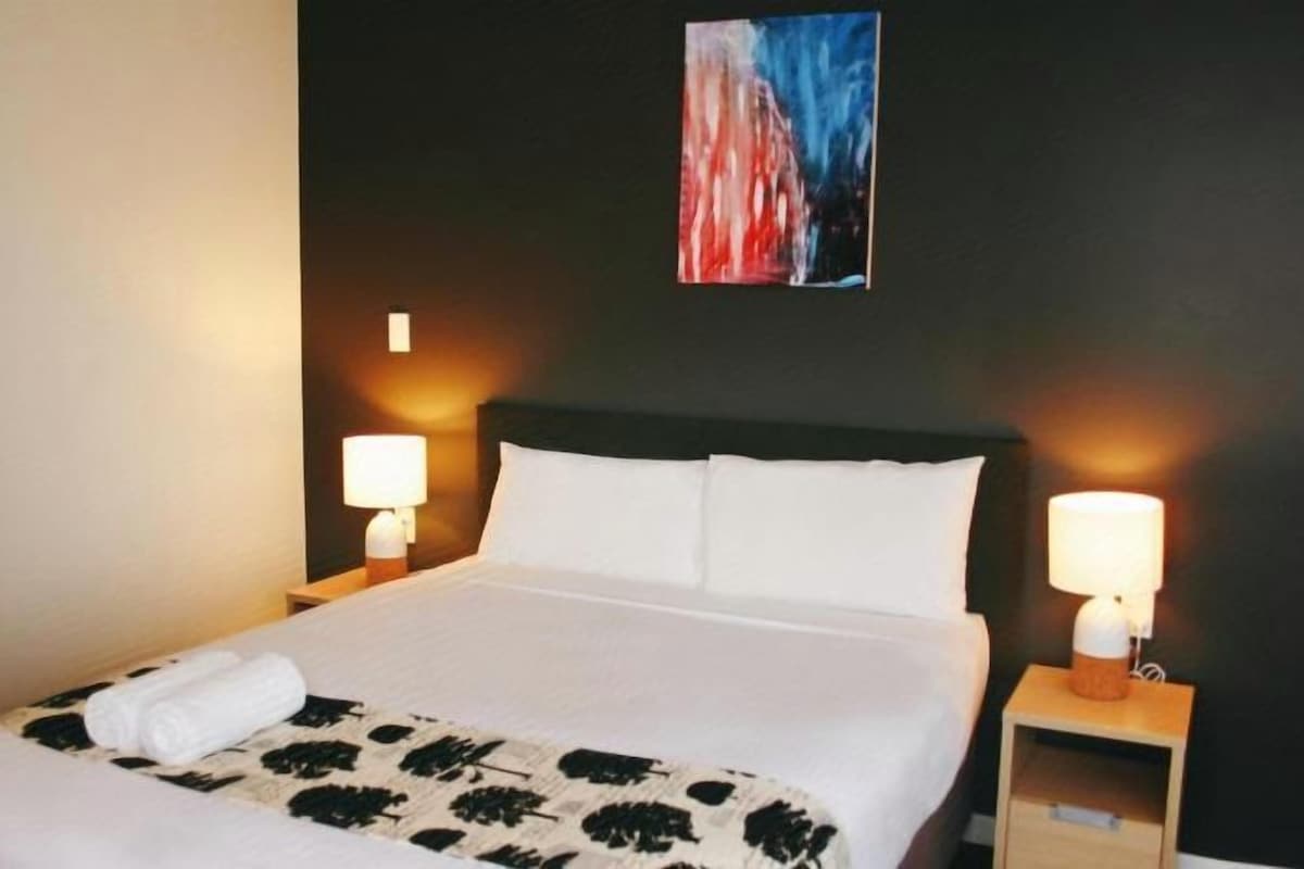 A hotel room with a bed, two bedside lamps, and a painting on the wall.