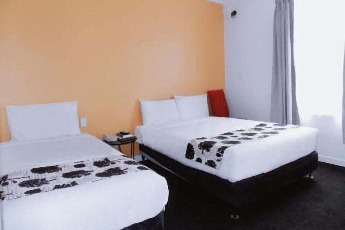 A hotel room with two beds, a nightstand, and a window with curtains.
