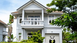 Een villa met twee verdiepingen, een balkon, een garage en weelderige begroeiing.
