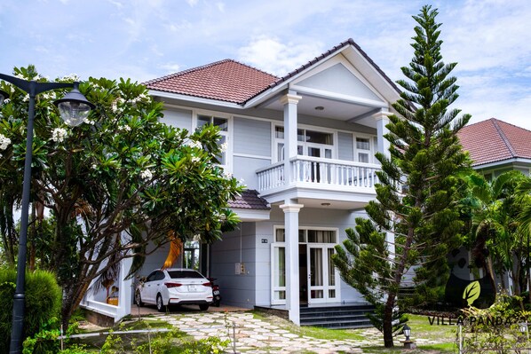 A two-story house with a balcony, a car parked in front, and a well-maintained garden.