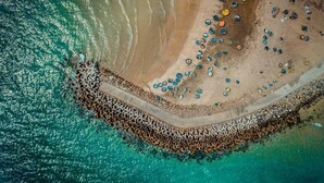 Luchtbeeld van een strand met een rotsenrijke zeewering en verspreide objecten.