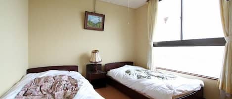 A room with two single beds, a nightstand with a lamp, a framed picture on the wall, and a window with curtains.