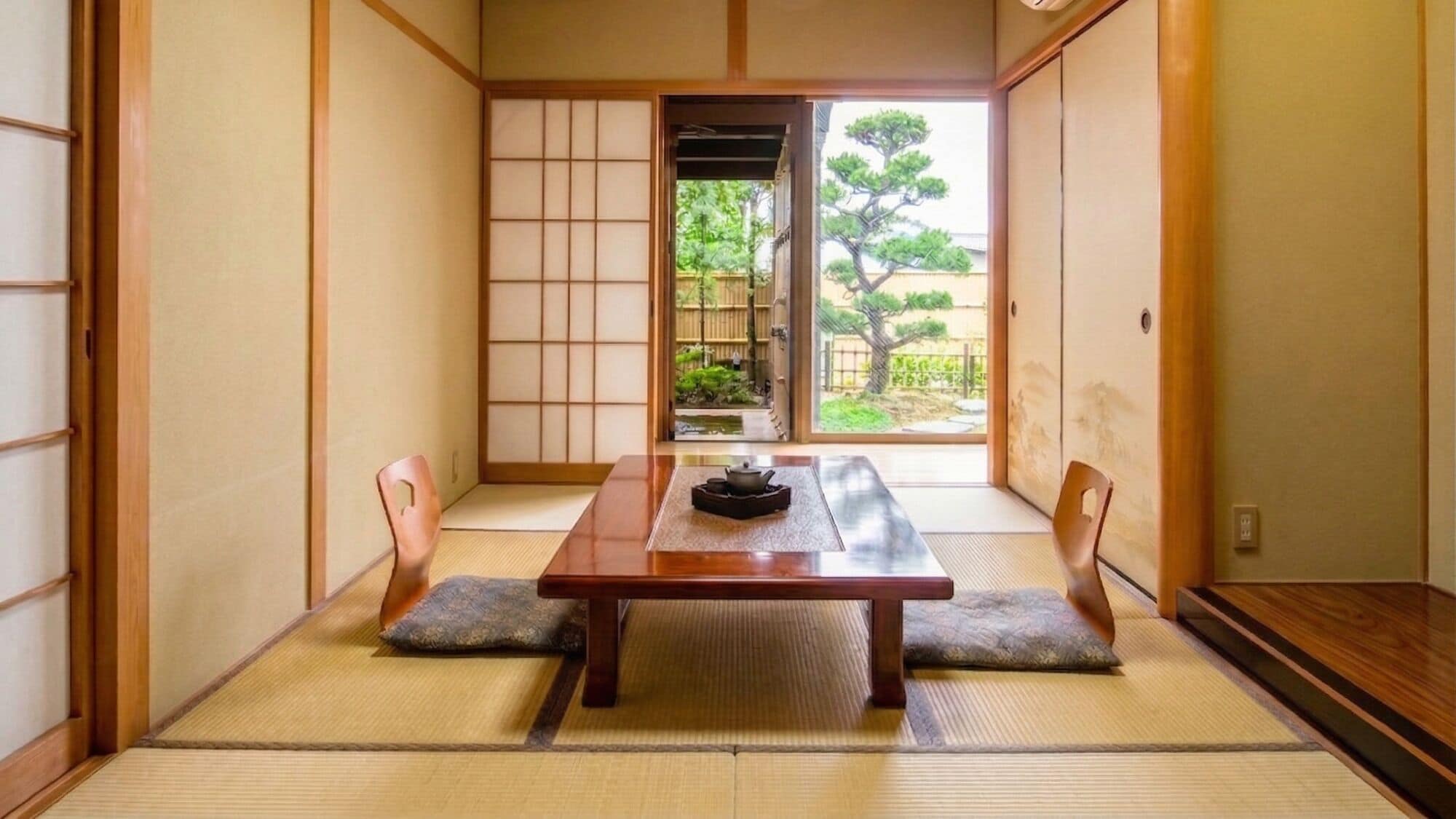 Una habitación japonesa tradicional con suelo de tatami, una mesa baja y puertas correderas que dan a un jardín.