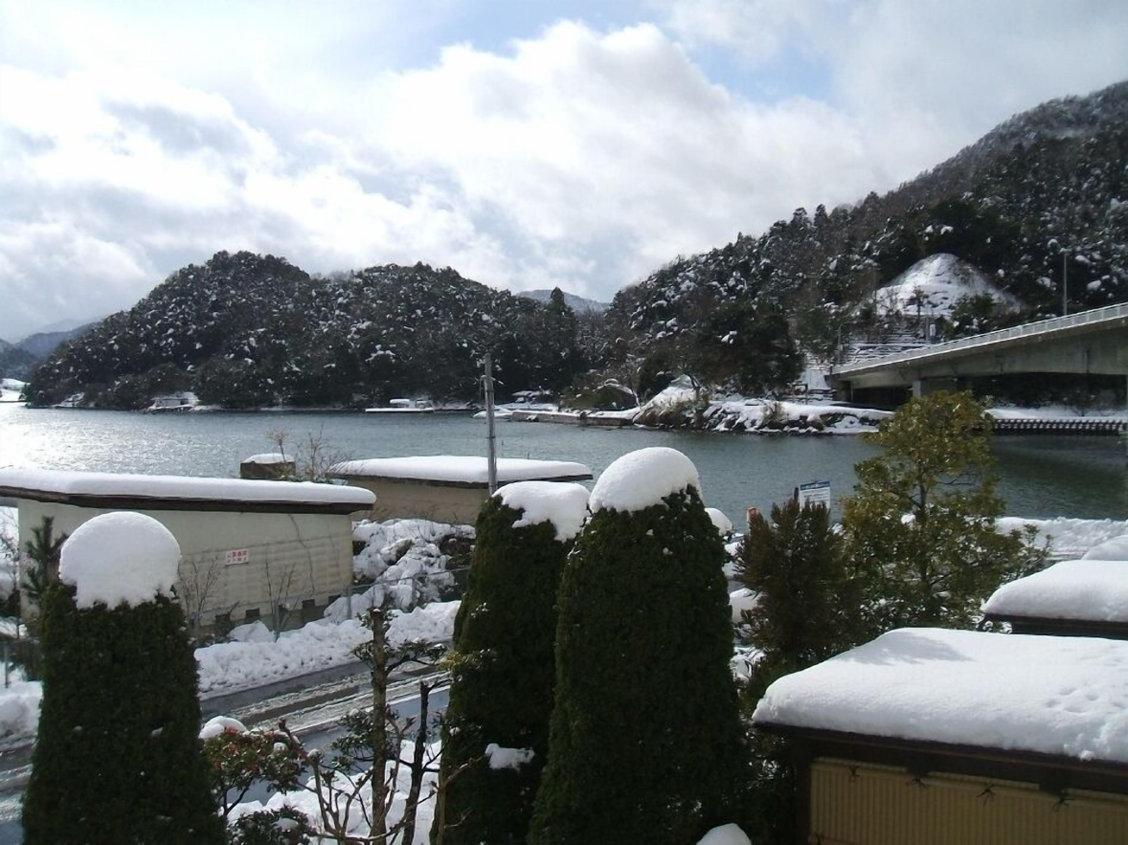 A snow-covered landscape with a bridge, trees, and a body of water.