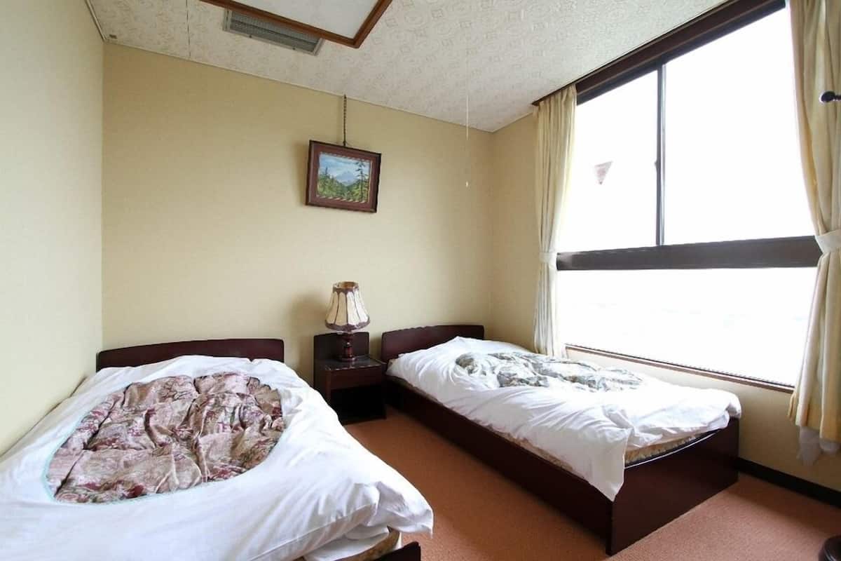 A room with two beds, a nightstand with a lamp, a framed picture on the wall, and a window with curtains.