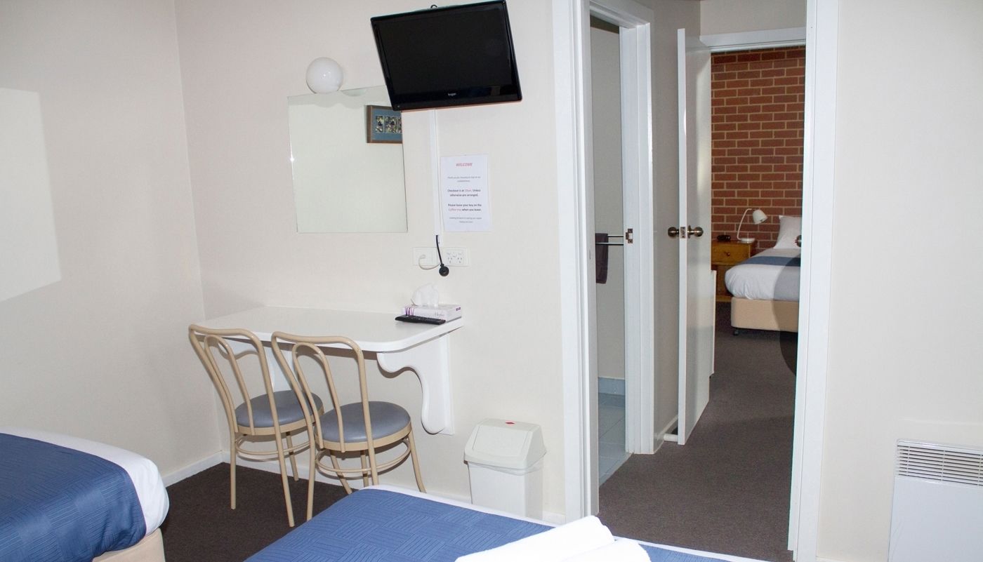 A hotel room with two beds, a desk with a chair, a television, and a door leading to a bathroom.