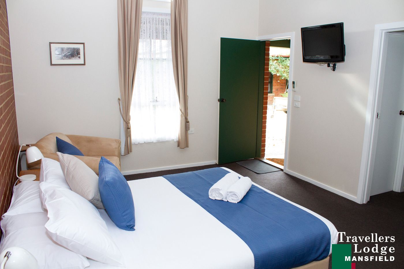 Habitación de hotel con una cama, un televisor y una puerta que da al exterior.