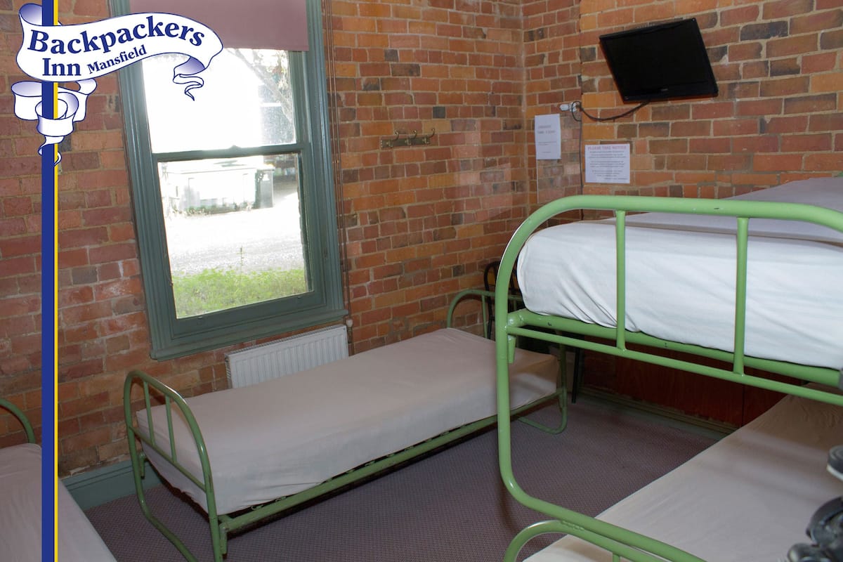 A room with two bunk beds, a window with a view, a brick wall, and a television mounted on the wall.