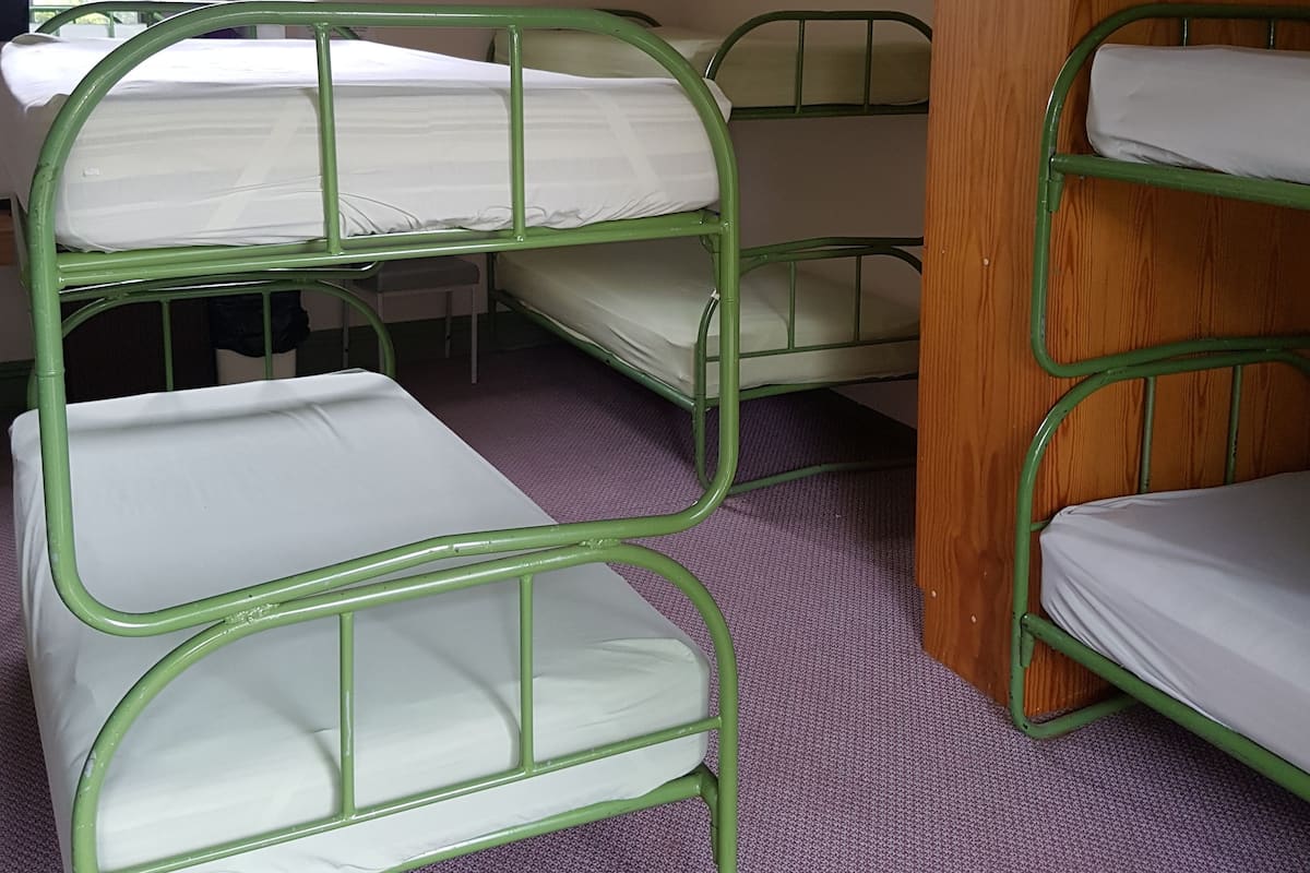 A dormitory room with bunk beds, a wooden wardrobe, and a window.