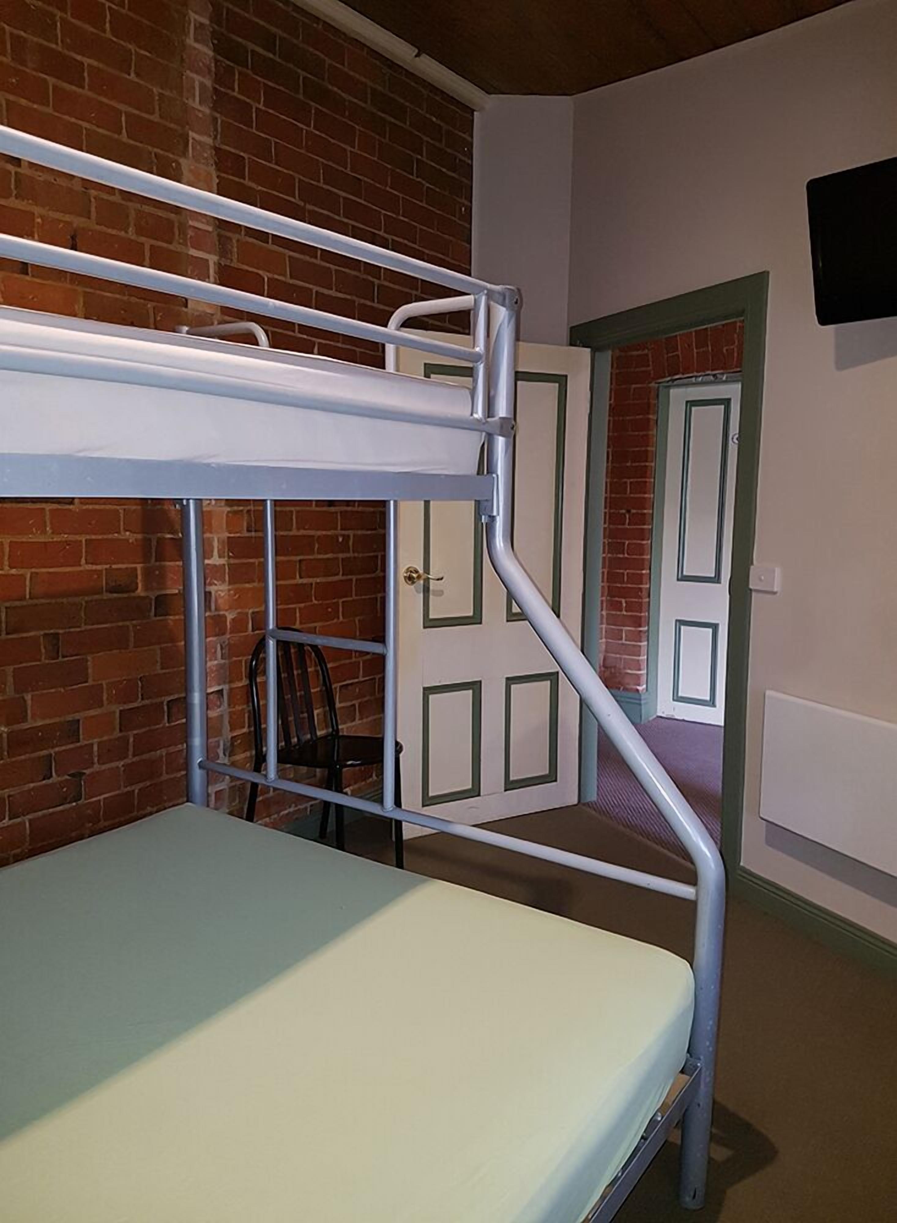 A bunk bed in a room with a brick wall and a door.