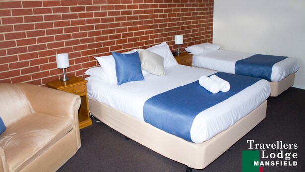 Habitación doble con dos camas, cada una con ropa de cama blanca y azul, un sillón color beige y una pared de ladrillo.