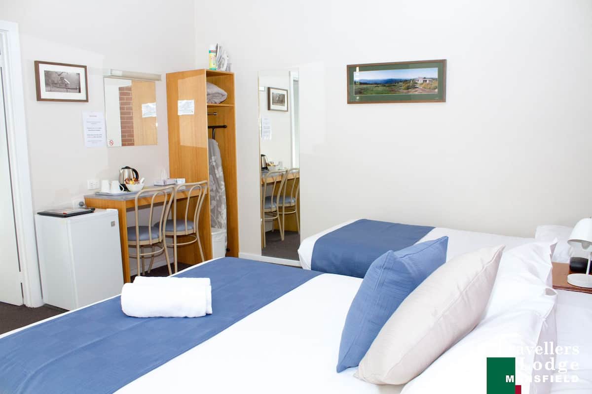 A hotel room with a bed, a desk, a chair, and a wardrobe. There is a framed picture on the wall.