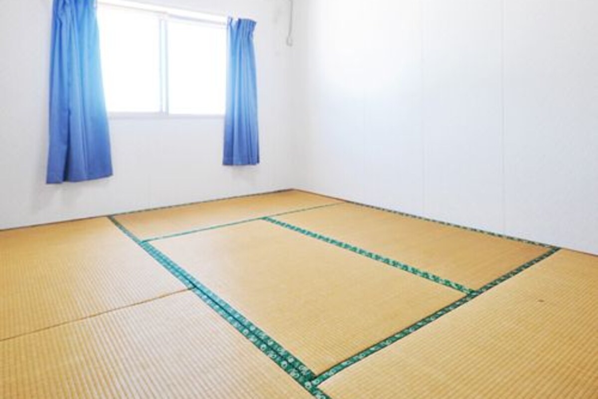 A room with tatami mat flooring, a window with blue curtains, and an air conditioning unit on the wall.