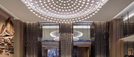 A spacious lobby with a modern chandelier, a reception desk, and a decorative wall.