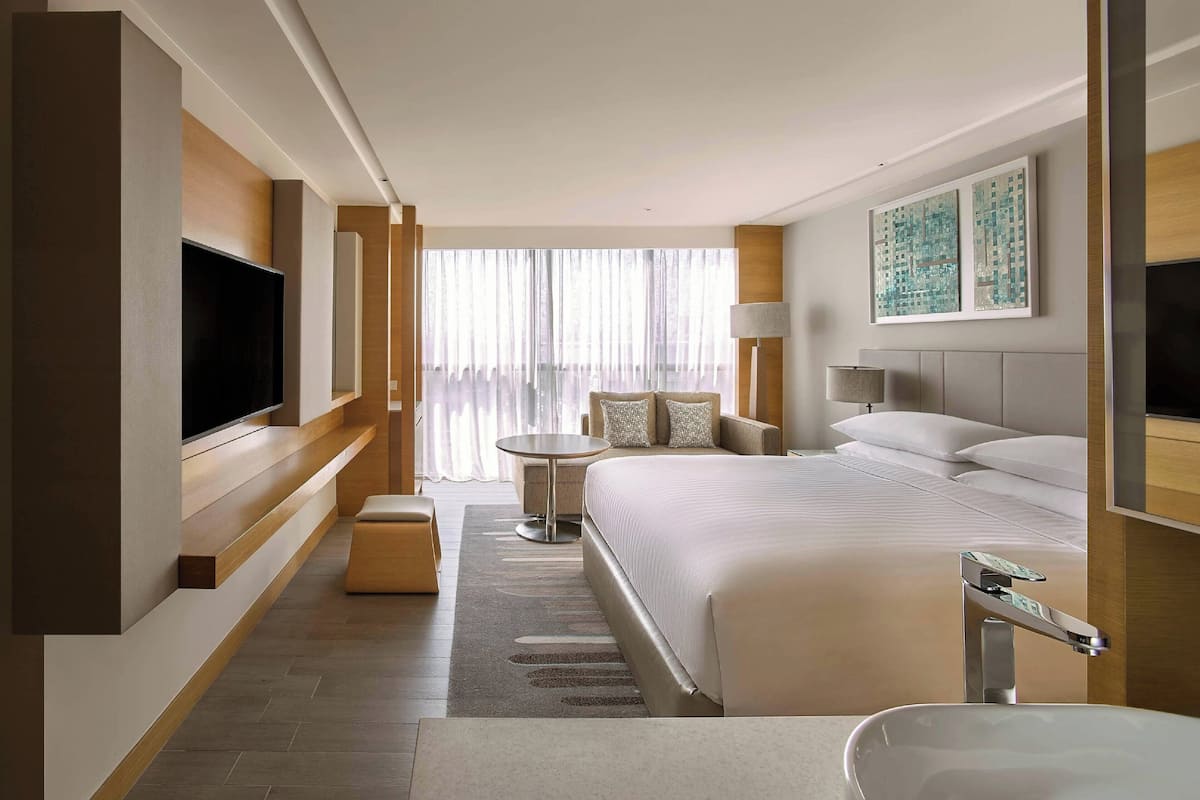 Une chambre d’hôtel moderne avec un grand lit, un téléviseur à écran plat fixé au mur, une petite table ronde et une salle de bain équipée d’un lavabo et d’un miroir.