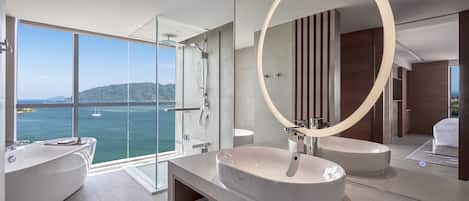 A modern bathroom with a large window, a bathtub, two sinks, and a circular mirror.