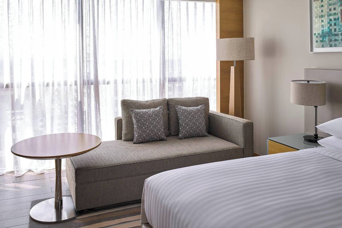 Une chambre d’hôtel avec un lit, un canapé agrémenté de coussins à motifs, une petite table ronde et une lampe.