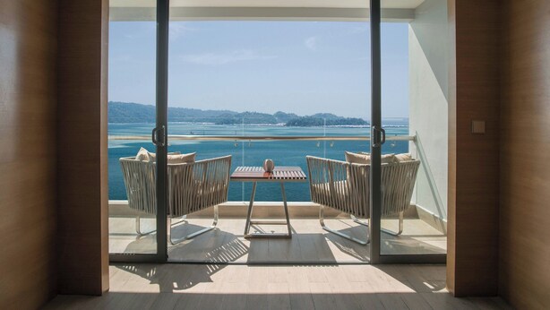 Un balcón con mesa y sillas, con vista al mar y la costa lejana.