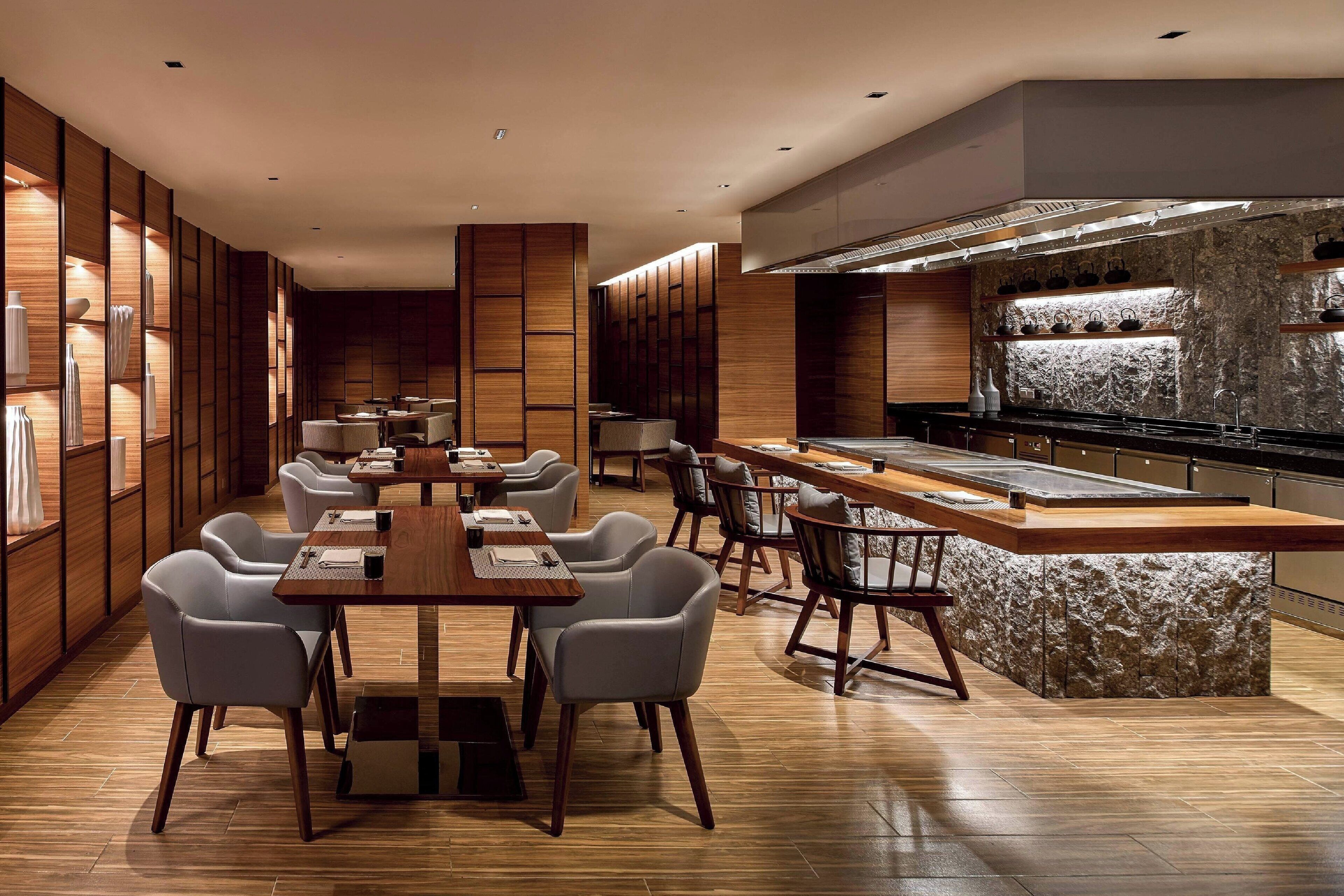 A modern dining area with wooden paneling, a central island with a stone backsplash, and a kitchen with a stone countertop and overhead ventilation.