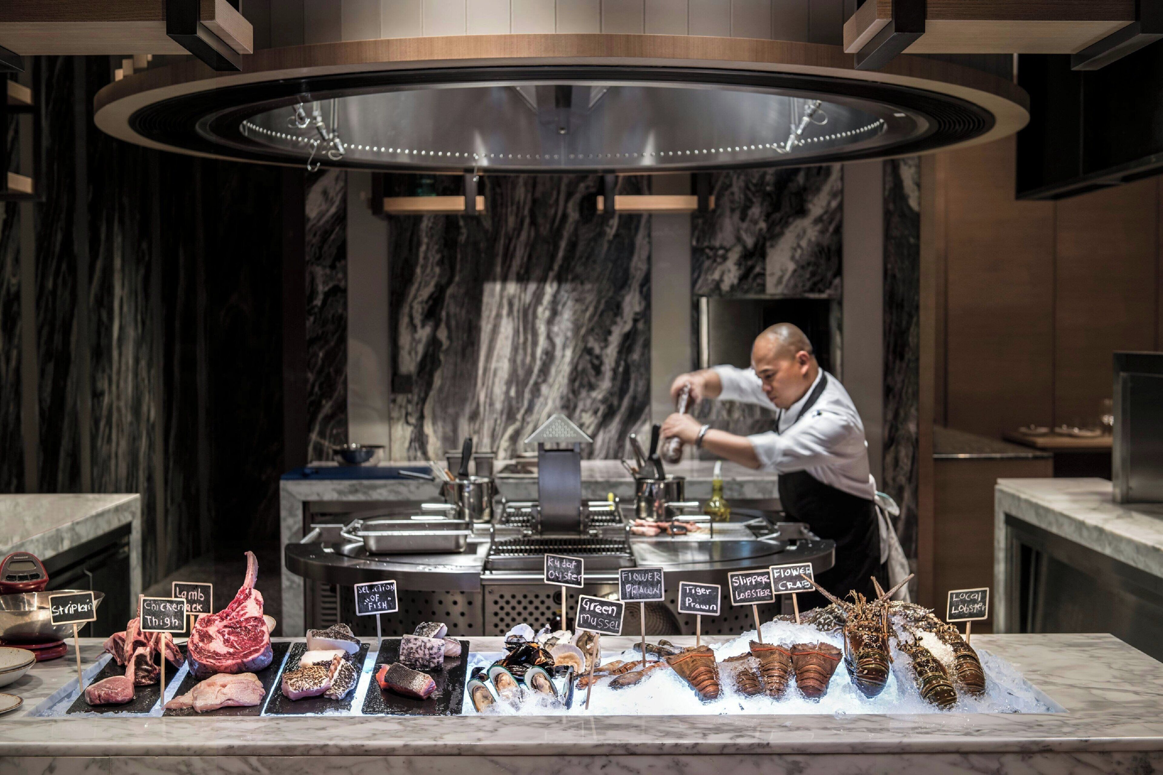 A seafood display with various types of fish and seafood, a chef preparing food, and a modern kitchen setting.