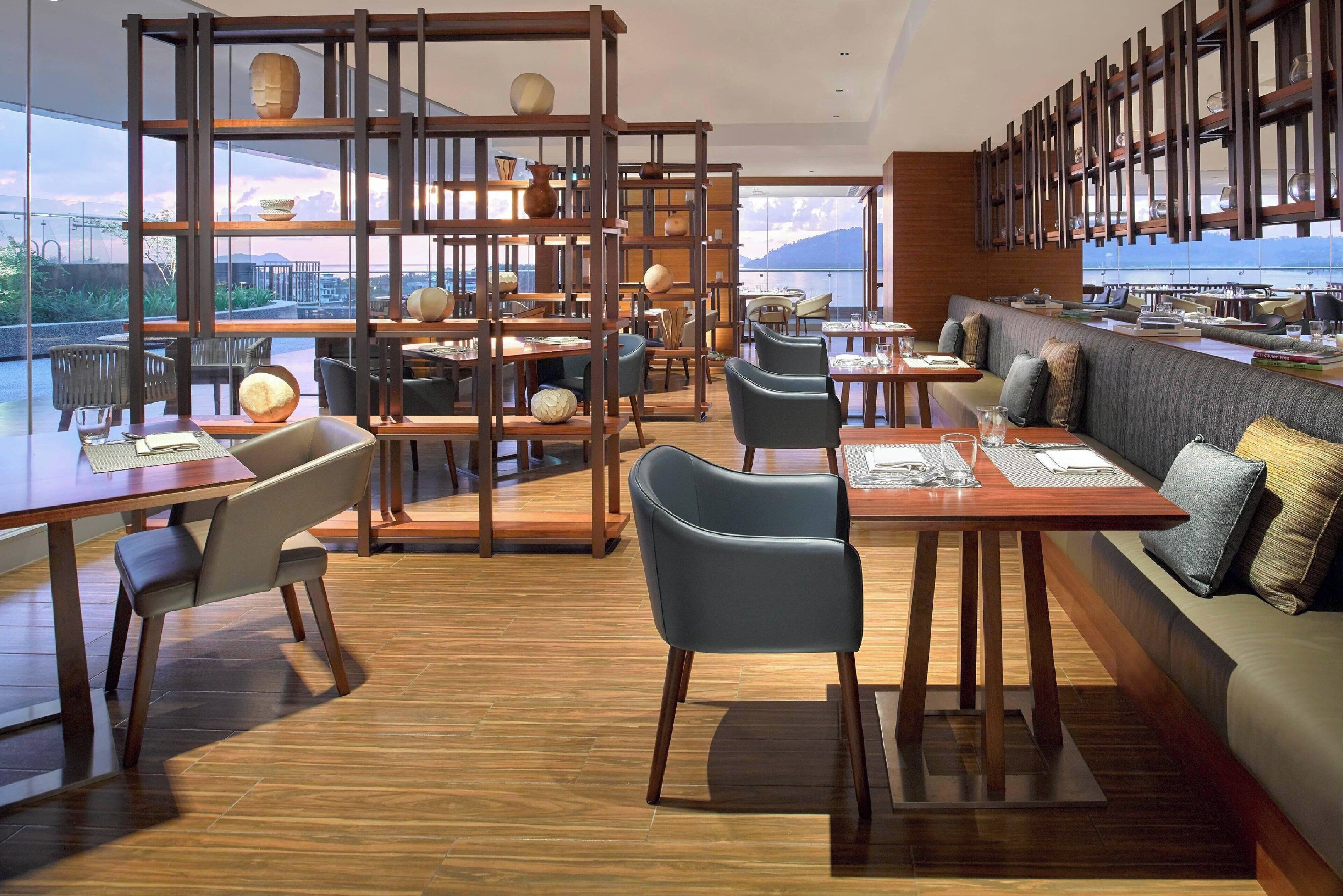 A modern restaurant with wooden furniture, a high ceiling, and large windows offering a view of the mountains.