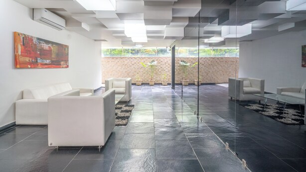 Um interior moderno com piso de azulejos, sofás brancos, divisória de vidro e parede de tijolos com plantas.