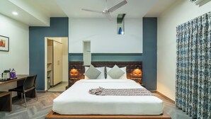Quarto de hotel com cama, escrivaninha, cadeira e ventilador de teto.