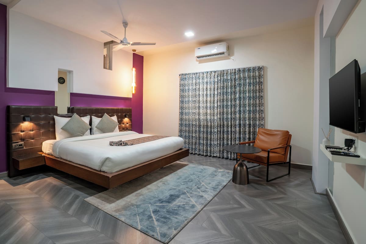 A modern hotel room with a bed, a chair, a TV, and an air conditioning unit.