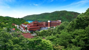 Un hotel de varios pisos con fachada de ladrillo rojo, rodeado de abundante vegetación y colinas.