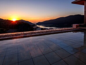 Una piscina en la azotea con vistas a un atardecer sobre un lago y colinas.