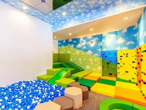 Zona infantil con piscina de pelotas, paredes de escalar y asientos acolchados.