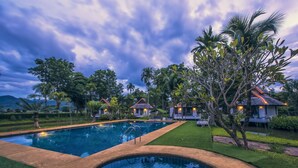A swimming pool surrounded by lush greenery and small houses with tiled roofs. - Bura Lumpai (Pai)