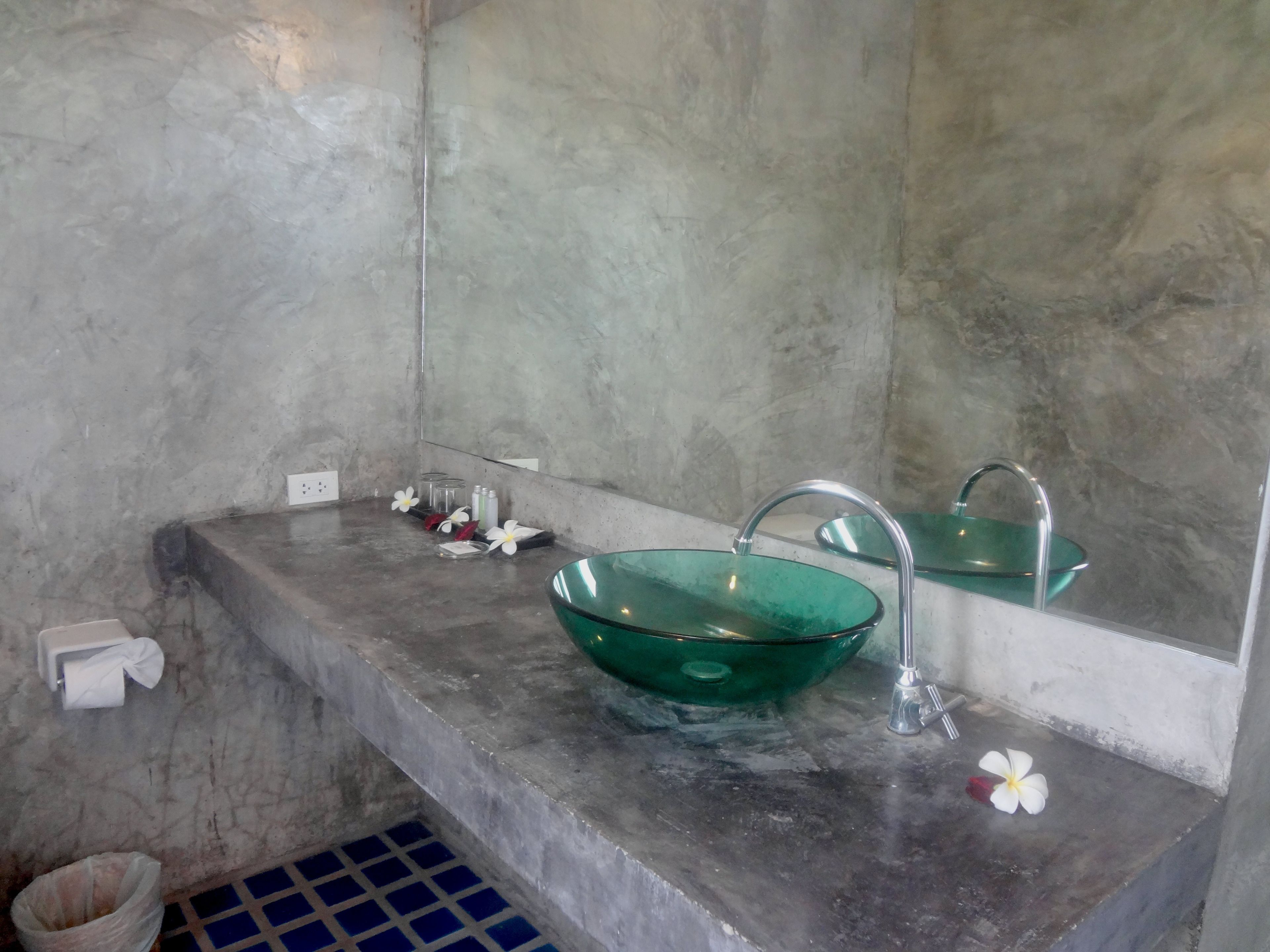 A bathroom with a green glass sink, a mirror, and a towel dispenser.