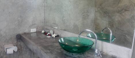 A bathroom with a green glass sink, a mirror, and a towel dispenser.
