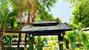 A traditional wooden pavilion with a tiled roof, surrounded by lush greenery and a pathway leading to a building with a balcony. - Bura Lumpai (Pai)