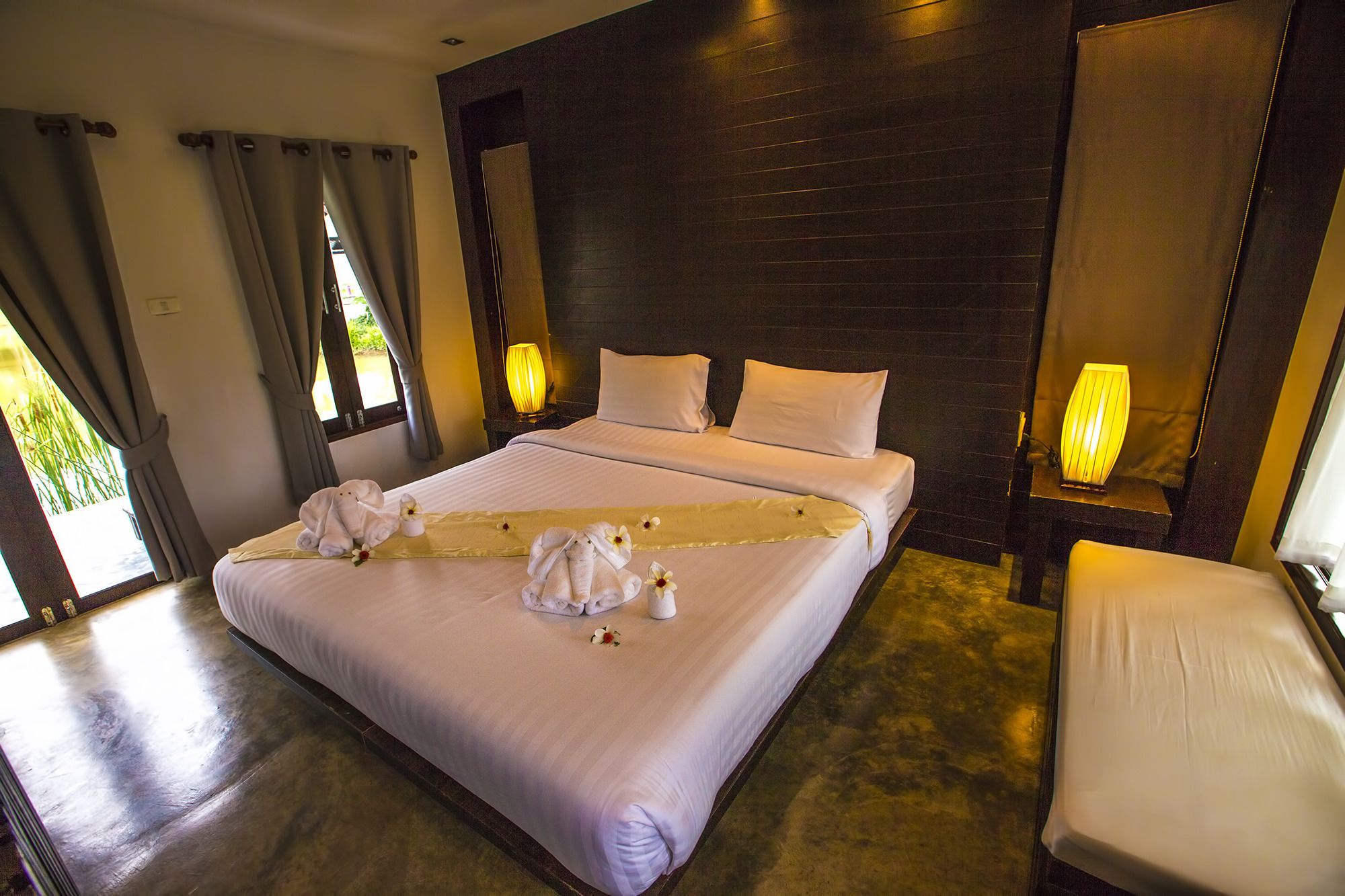 A hotel room with a large bed, two bedside lamps, a chair, and a view of greenery outside.
